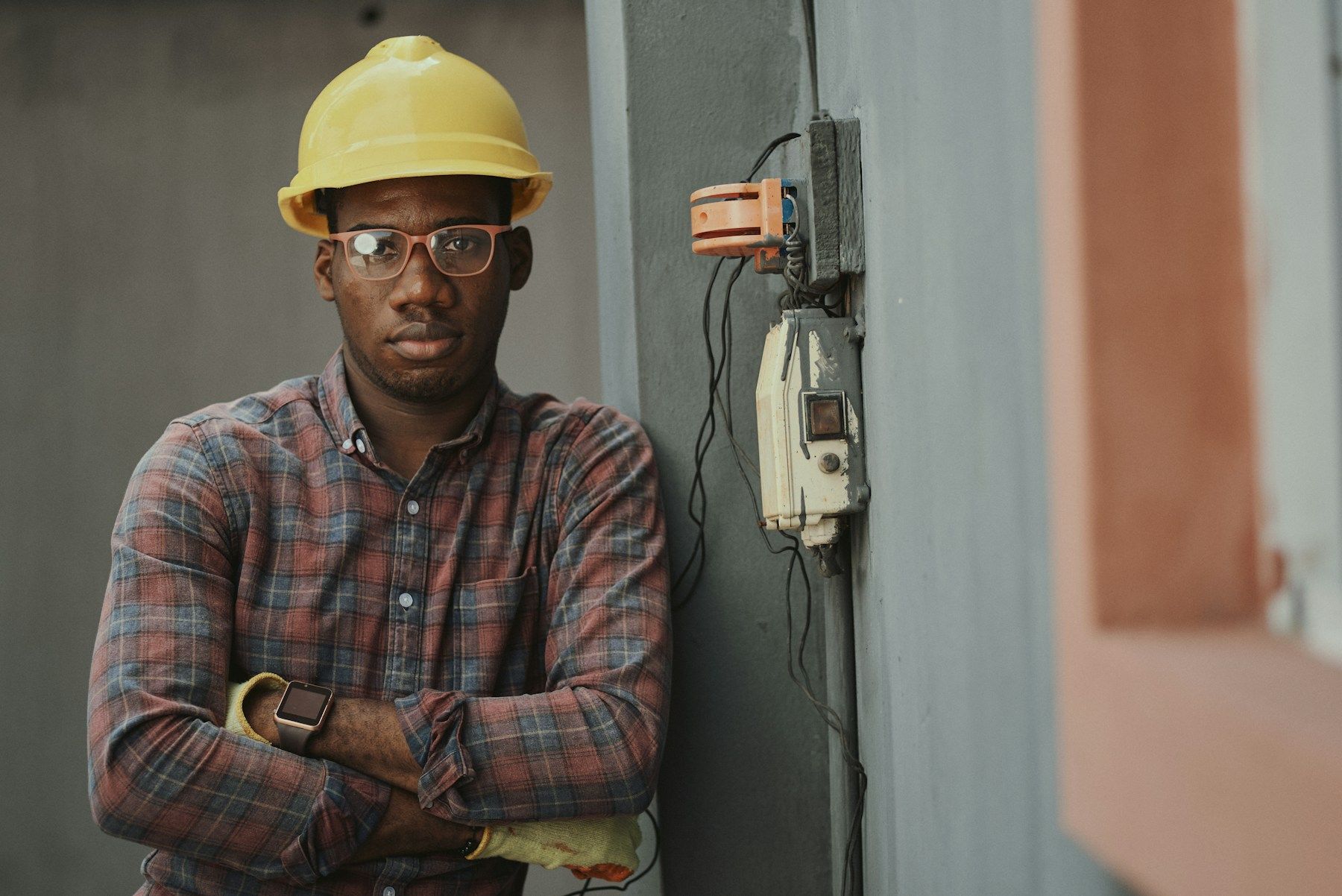 A tradesperson in a hard hat standing with his arms crossed beside an electrical panel