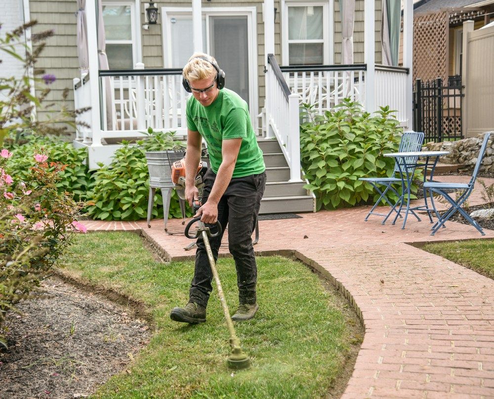 A landscaper trimming a lawn in front of a house