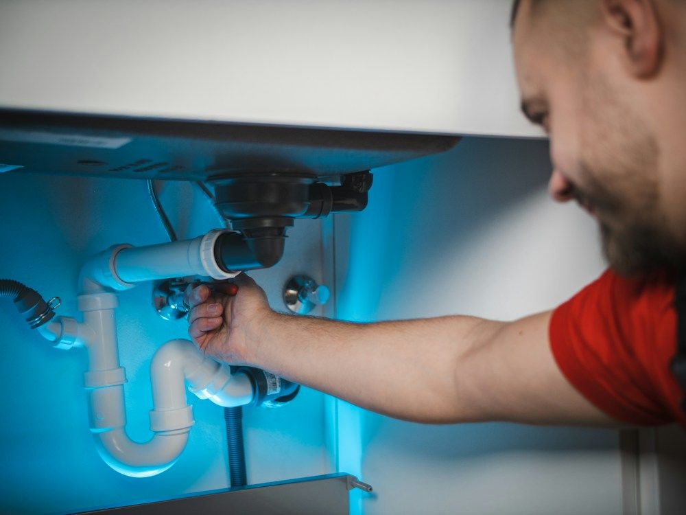 A plumber fitting a pipe under a sink